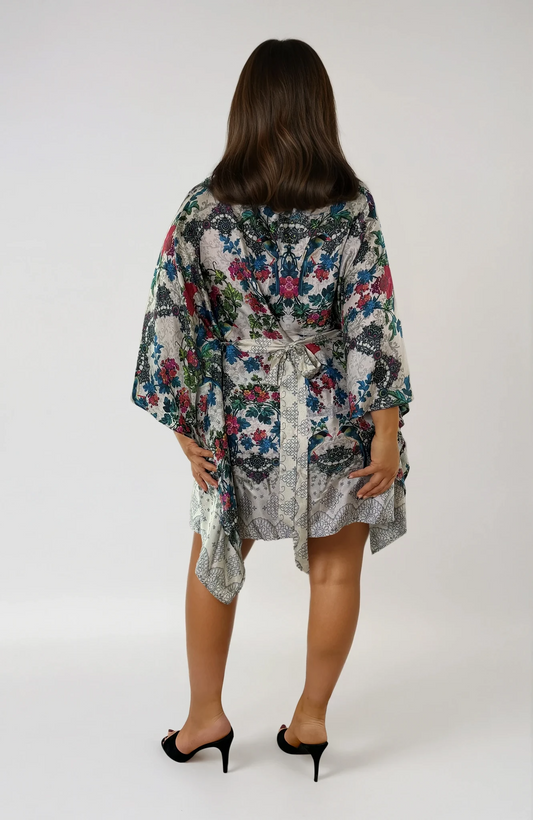 Back view of the ZALA silk kaftan dress in Secret Garden, featuring an ivory ground adorned with painterly florals in soft teal, berry, rose, and sage tones. Inspired by antique botanical textiles, the intricate pattern evokes timeless romance, artistry, and effortless elegance. The removable sash is tied at the back to softly define the waist, while flowing draped sleeves and an asymmetrical hem create graceful movement from every angle.