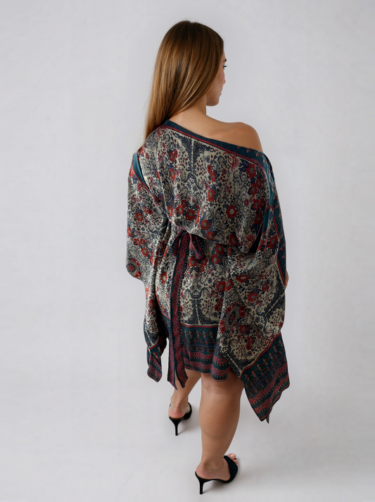 Back view of the ZALA rayon kaftan dress in Heirloom Blue, featuring a white ground adorned with intricate floral motifs, ornamental detailing, rich blue borders, and subtle berry accents inspired by heirloom textiles. Styled slightly off one shoulder to showcase the versatile boat neckline, with the sash tied at the back and draped sleeves creating an effortlessly elegant silhouette.