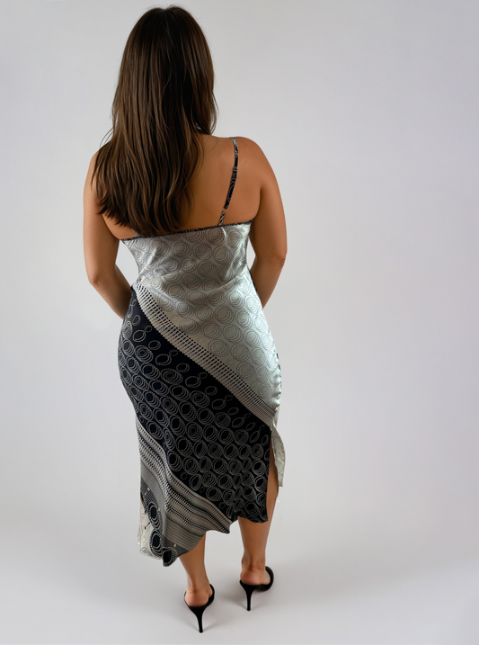 Back view of the CORA Silk Slip Dress in Ivory Eclipse. Bias-cut silk charmeuse midi dress with adjustable straps and side slits. The engineered black-and-ivory geometric print features sweeping diagonal panels, circular motifs, and intricate border details that create elegant visual movement.