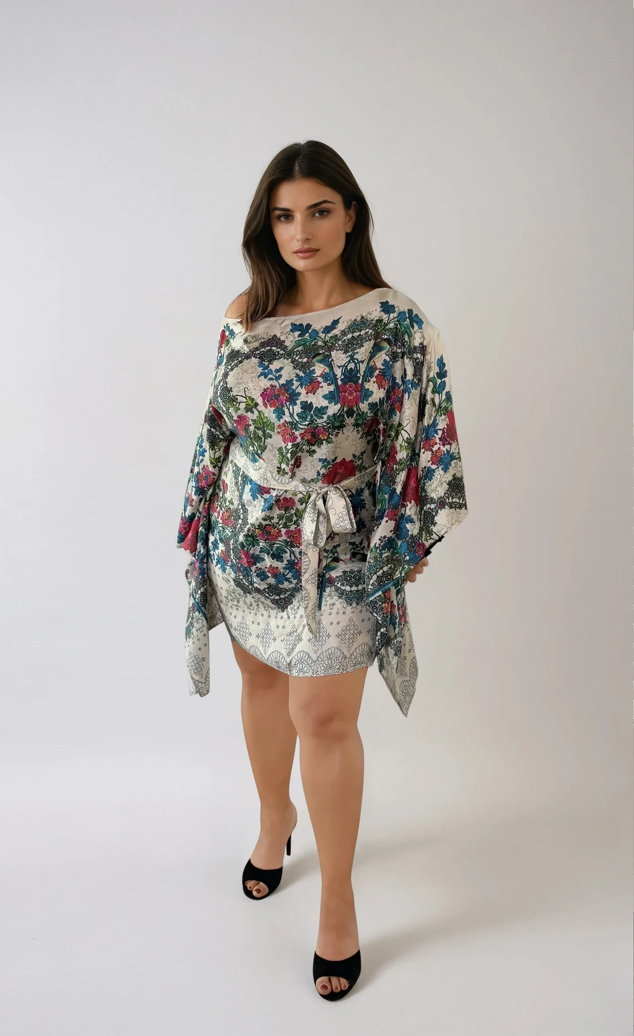 Front view of the ZALA silk kaftan dress in Secret Garden, featuring an ivory ground adorned with painterly florals in soft teal, berry, rose, and sage tones. Inspired by antique botanical textiles, the intricate pattern evokes timeless romance, artistry, and effortless elegance. Styled with the sash tied at the front to softly define the waist and worn slightly off one shoulder to showcase the versatile boat neckline and fluid draped sleeves.