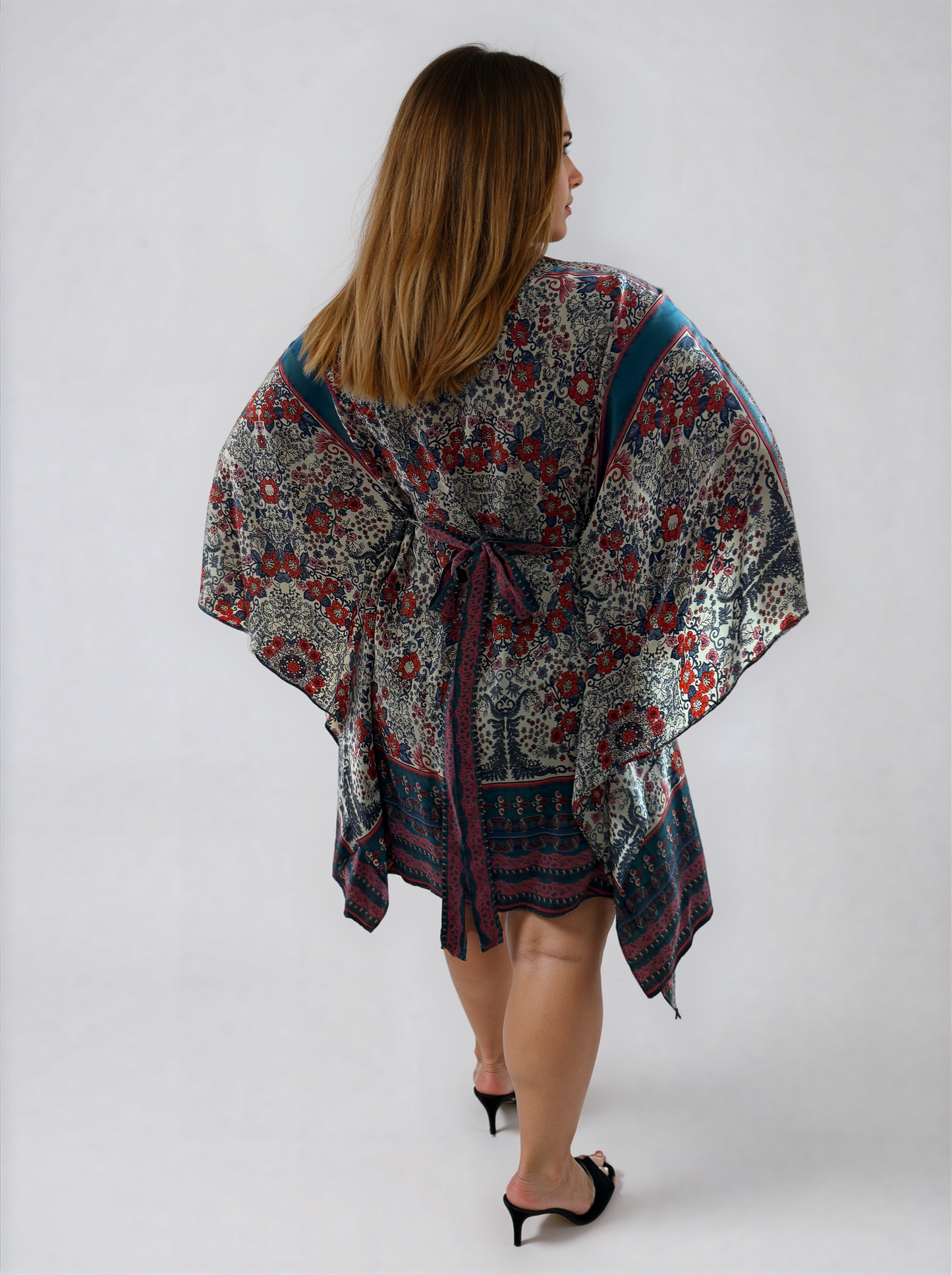 Back view of the ZALA rayon kaftan dress in Heirloom Blue, featuring a white ground adorned with intricate floral motifs, ornamental detailing, rich blue borders, and subtle berry accents inspired by heirloom textiles. The removable sash is tied at the back to softly define the waist, while flowing draped sleeves create an asymmetrical hem allowing for graceful movement from every angle.